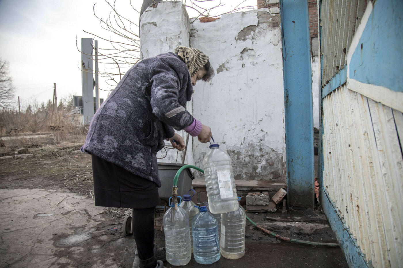 Starsza osoba zbiera wodę w plastikowych butelkach z kranu na zewnątrz fabryki częściowo zniszczonej na obrzeżach Torecka, foto: Narciso Contreras / Anadolu