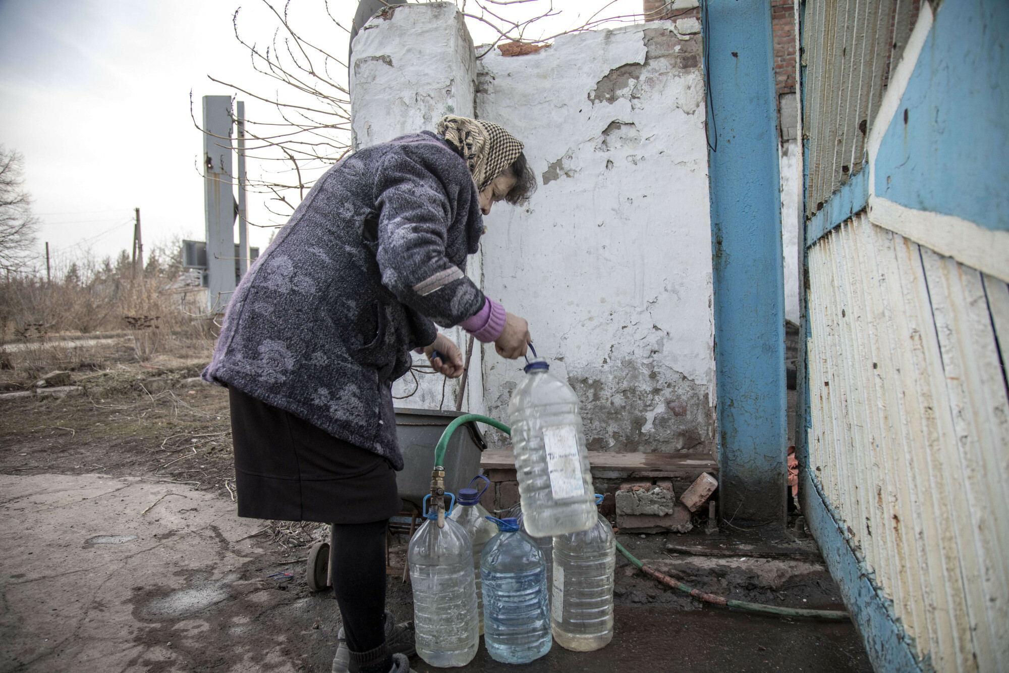 Starsza osoba zbiera wodę w plastikowych butelkach z kranu na zewnątrz fabryki częściowo zniszczonej na obrzeżach Torecka, foto: Narciso Contreras / Anadolu